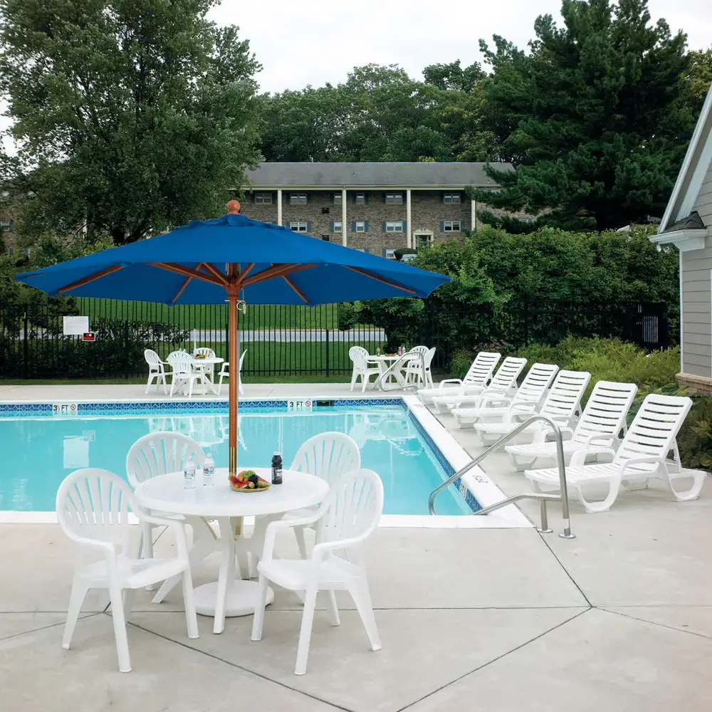 Apartment community pool featuring white Bahia chaise lounges and a blue Windmaster umbrella shading an the Pacific Fanback dining set.